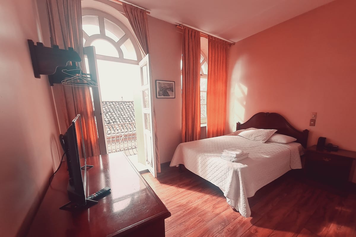 Un dormitorio con cama de madera, un escritorio con silla, una ventana con cortinas y vistas al exterior.