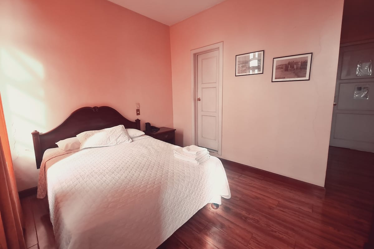 Un dormitorio con una cama, una mesita de noche, una puerta y dos cuadros en la pared.
