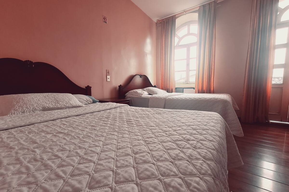 Una habitación de hotel con dos camas, suelo de madera y una ventana con cortinas.