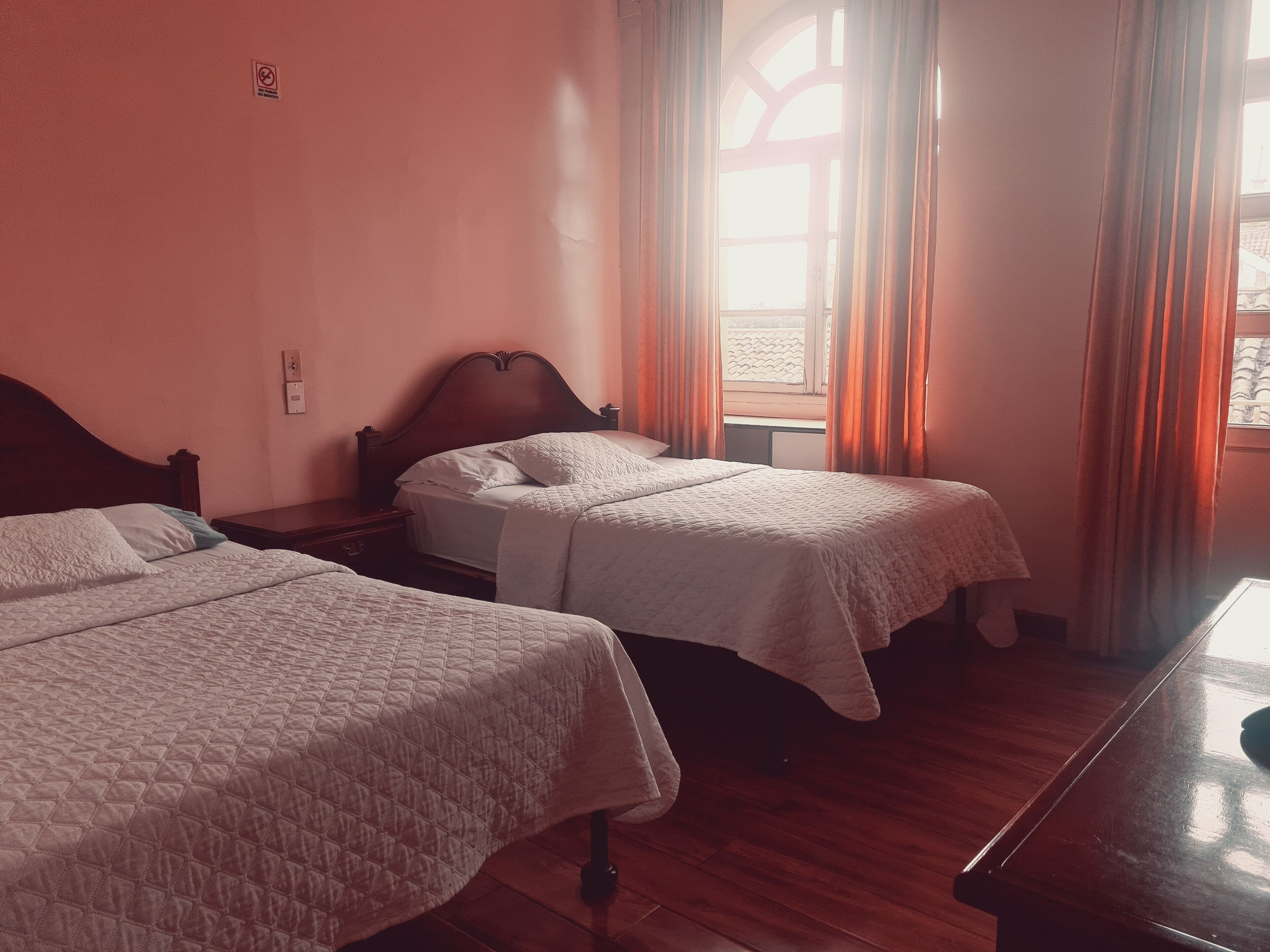 Una habitación con dos camas individuales, cabeceros de madera, una ventana con cortinas y suelo de madera.