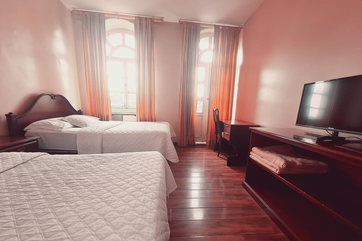 Una habitación de hotel con dos camas, un escritorio con computadora, televisión y ventana con cortinas.