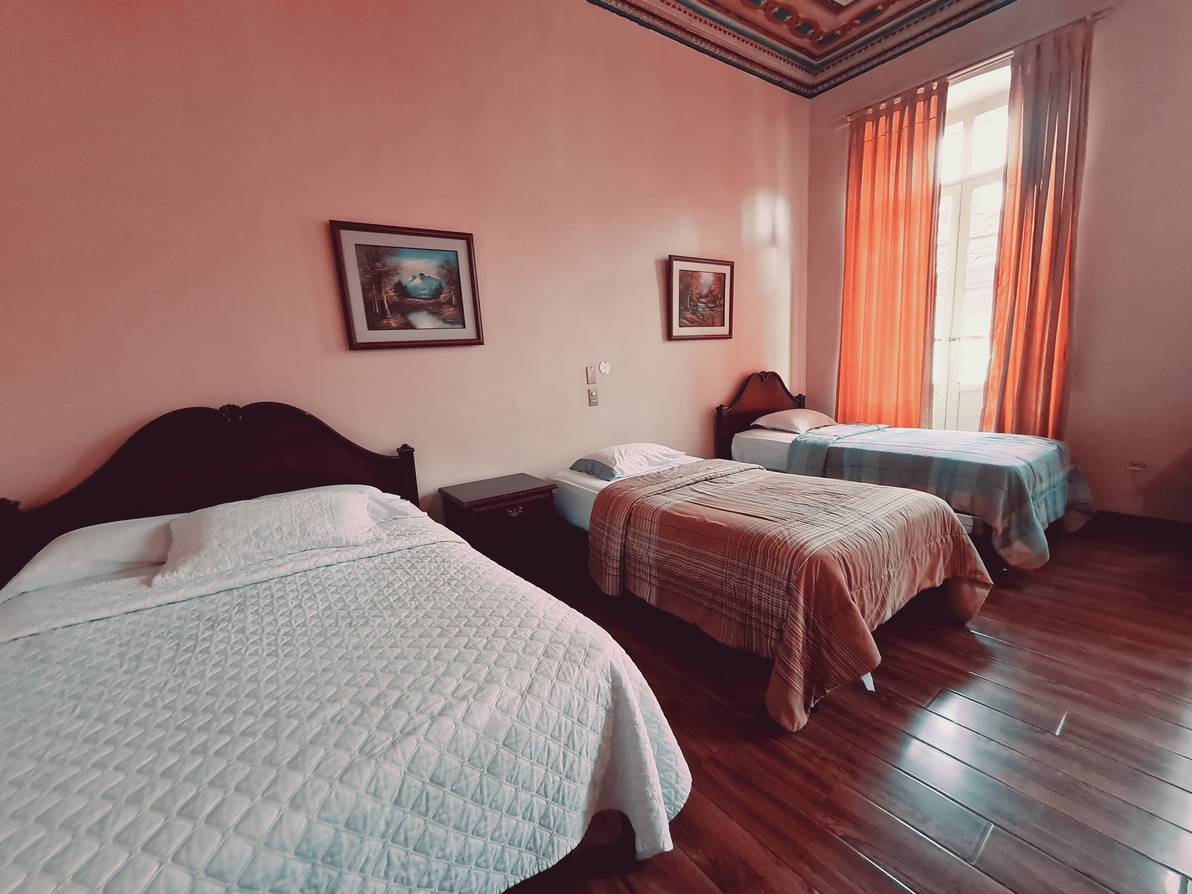 Una habitación con tres camas, piso de madera y dos cuadros en la pared.