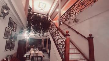 A staircase with ornate metal railings and wooden balusters, leading to a dining area with tables and chairs.