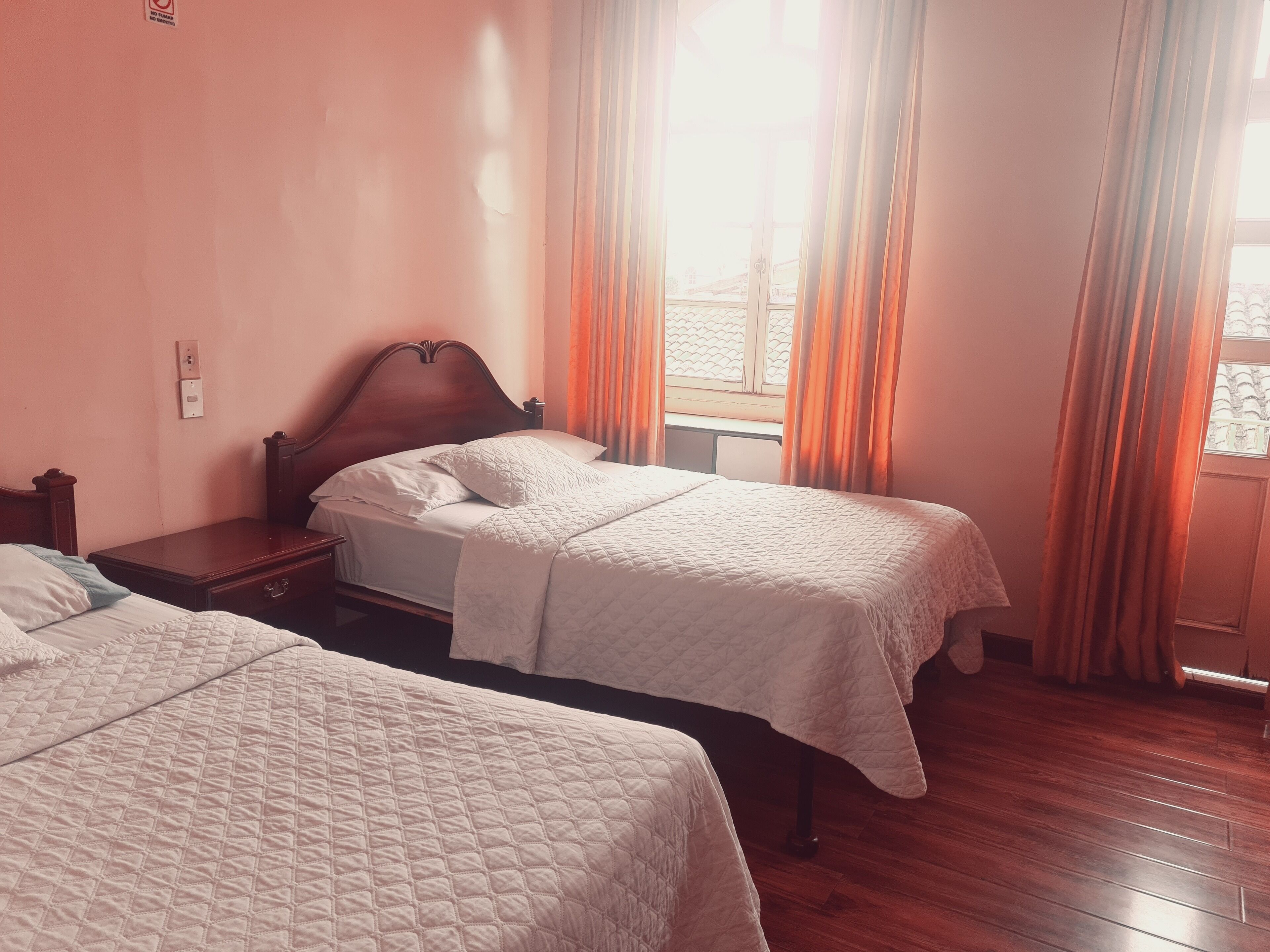 Quarto de hotel com duas camas, cabeceiras de madeira e uma janela com cortinas.
