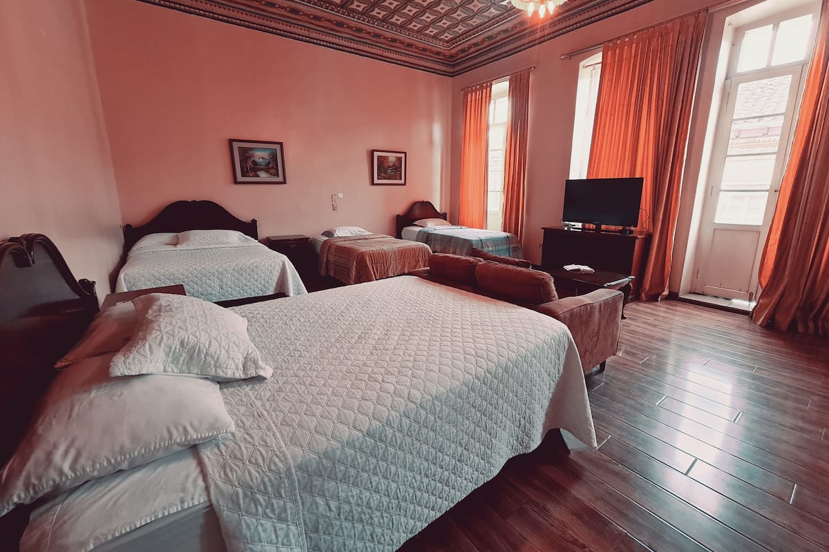 Habitación de hotel con tres camas, televisión y piso de madera.
