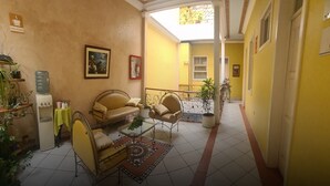 A sunlit room with yellow walls, a large window, a sofa, a coffee table, and a water dispenser. - Hotel Chat Noir Cuenca (Cuenca)