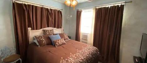 A bedroom with a bed, curtains, a ceiling fan, and a window.