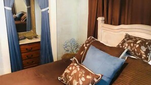 Un dormitorio con cama, cómoda, espejo y cortinas.