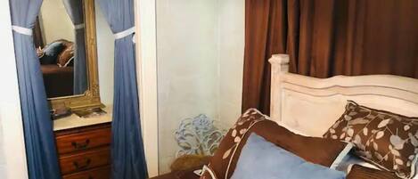 Un dormitorio con cama, cómoda, espejo y cortinas.