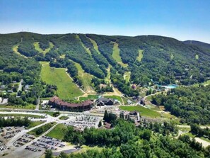 A large parking lot, a building with a red roof, and a mountainous landscape with winding paths.