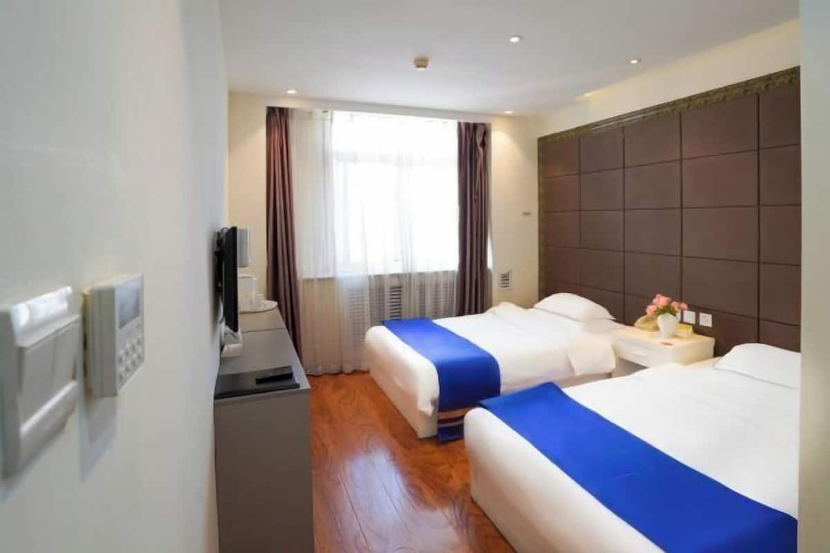 A hotel room with two beds, a TV, a small desk, and a window with curtains.
