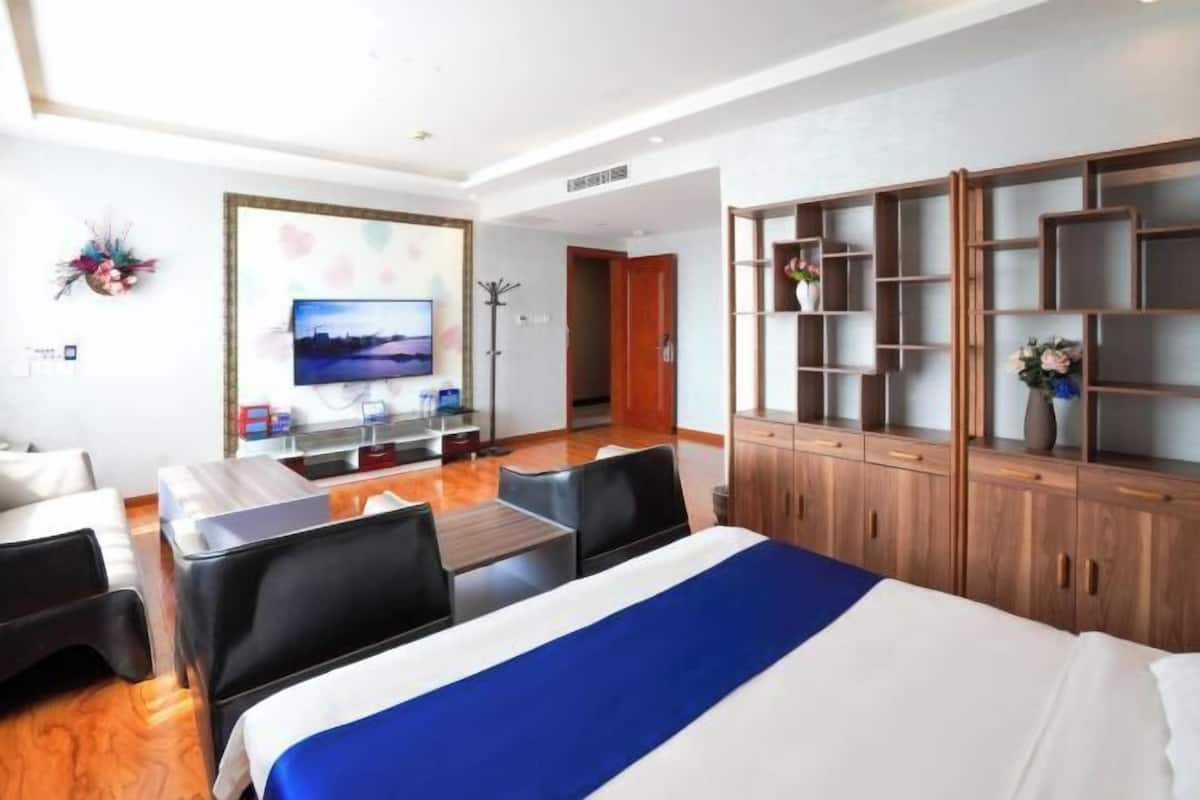 A hotel room with a bed, a desk, a chair, a TV, a wardrobe, and a shelf with decorative items.
