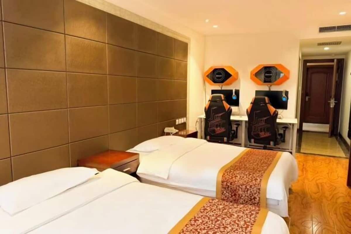 A hotel room with two beds, a large padded headboard, and two gaming chairs.