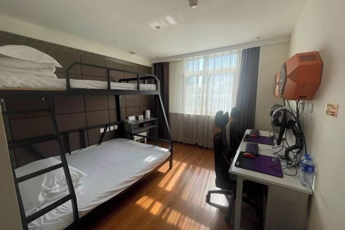 A room with bunk beds, a desk with a computer, and a window with curtains.