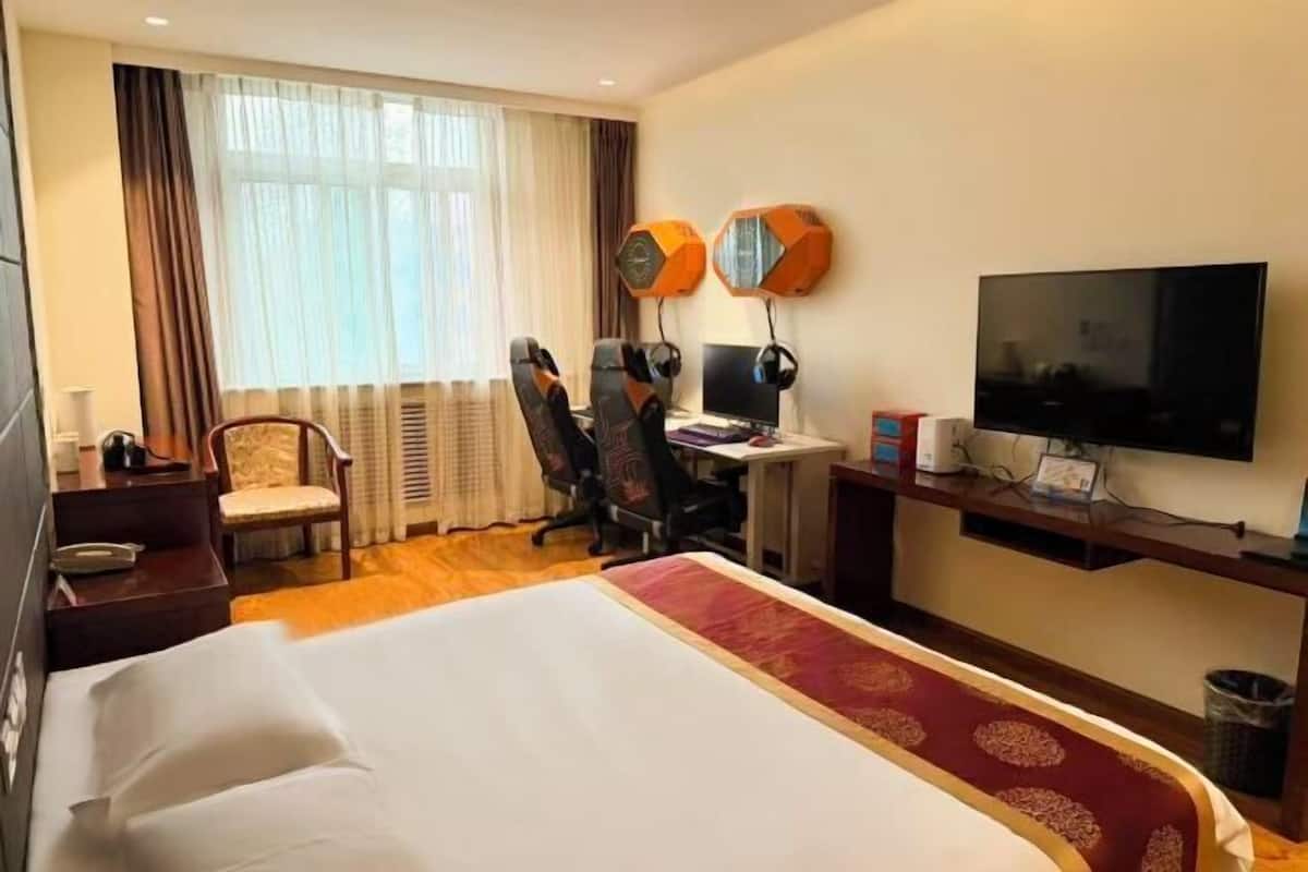 A hotel room with a bed, desk, chair, television, and a window with curtains.