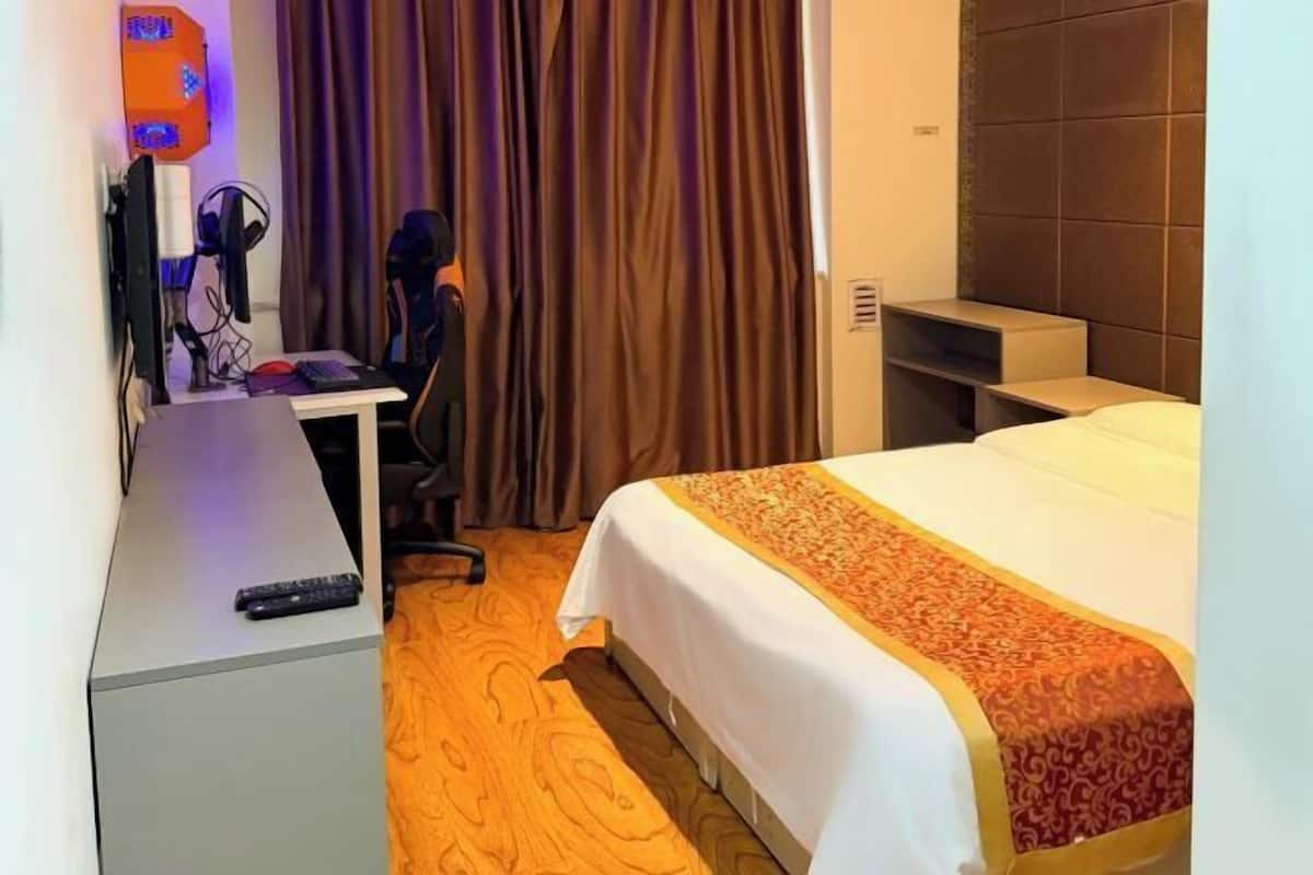 A hotel room with a bed, a desk with a computer, a chair, and a curtain.