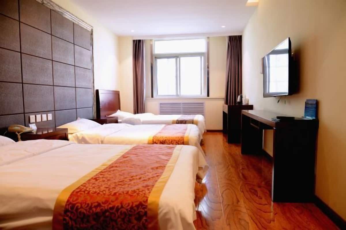 A hotel room with two beds, a television, a desk, and a window with curtains.