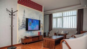 A living room with a flat-screen TV, a coat rack, a wooden coffee table, and two white leather sofas. - Junyi · Leishen Jingjie E-Sports Hotel (Beijing Yanqing Global Xinyi Department Store) (Beijing)
