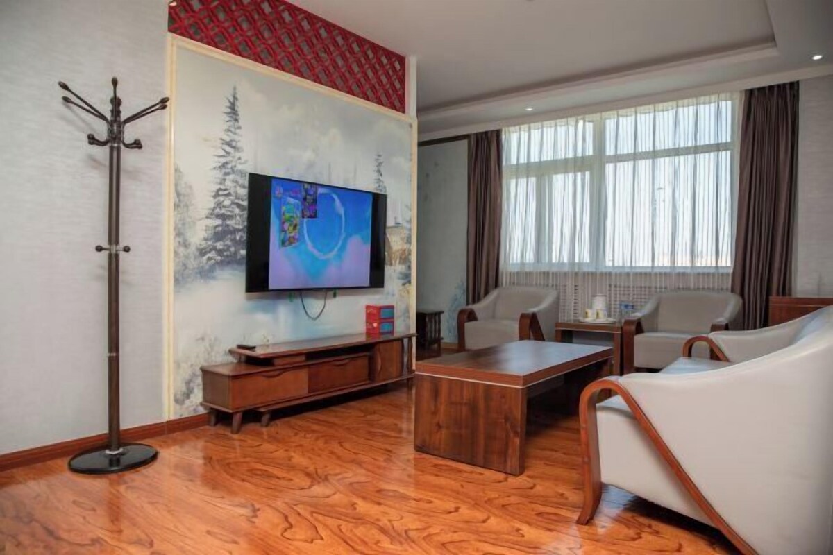 A living room with a flat-screen TV, a coat rack, a wooden coffee table, and two white leather sofas.