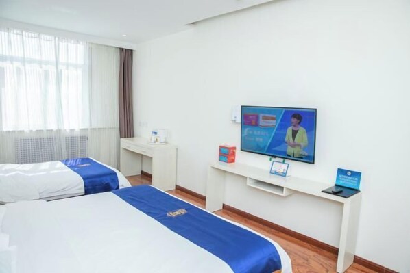 A hotel room with two beds, a desk, a television, and a small table with a sign.