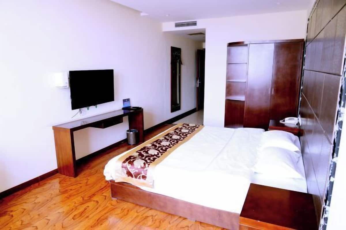 A hotel room with a bed, a TV mounted on the wall, a wooden desk, and a wardrobe.