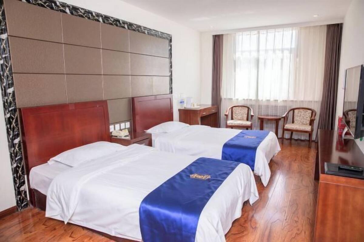 A hotel room with two beds, a desk, a chair, and a TV.