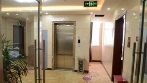 A hotel lobby with a marble floor, an elevator, a glass door, and a potted plant. - Junyi · Leishen Jingjie E-Sports Hotel (Beijing Yanqing Global Xinyi Department Store) (Beijing)