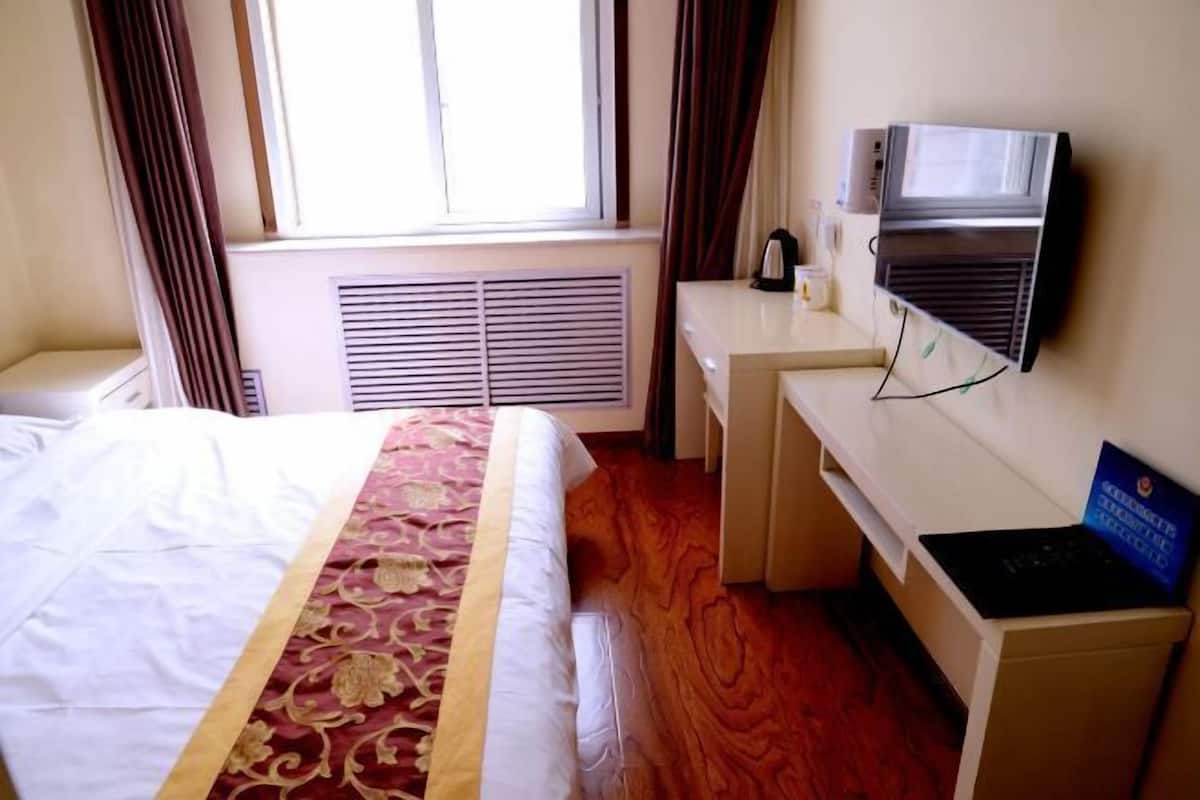 A hotel room with a bed, a desk, a television, and a window with curtains.