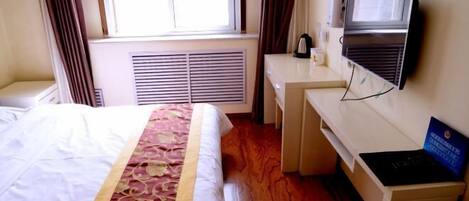 A hotel room with a bed, a desk, a television, and a window with curtains.