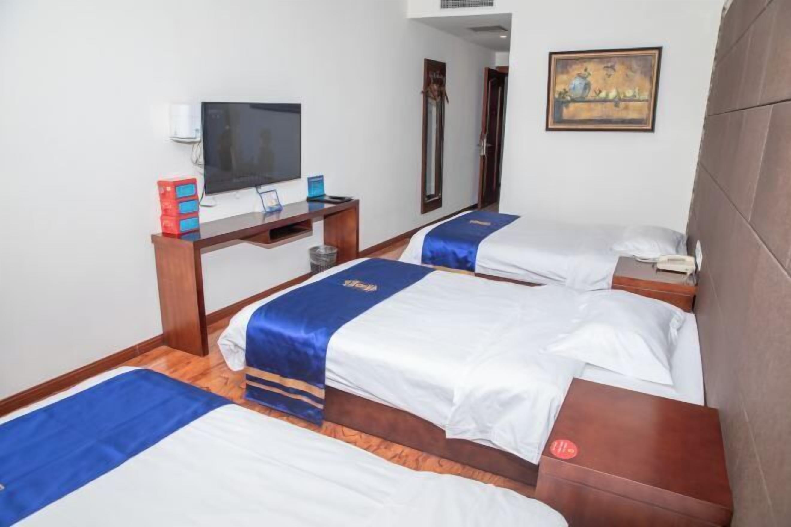 A hotel room with two beds, a TV, a desk, and a painting on the wall.
