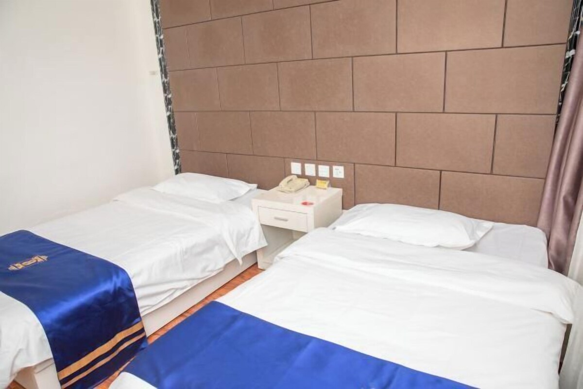A hotel room with two single beds, a bedside table with a telephone, and a wall-mounted light fixture.