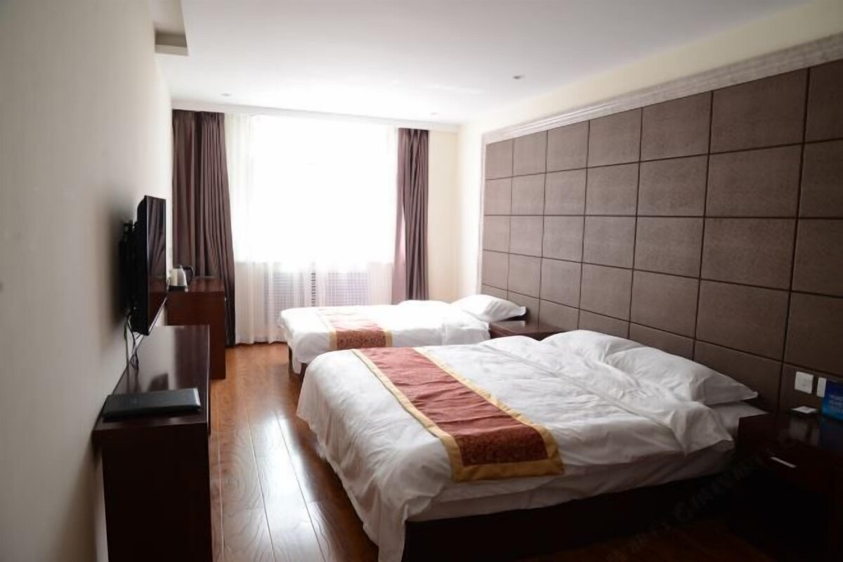 A hotel room with two beds, a television, and a window with curtains.