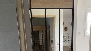 Een kamer met een houten vloer, een bed met beddengoed met een patroon, een wandplank met potten en een deur met een spiegelpaneel.