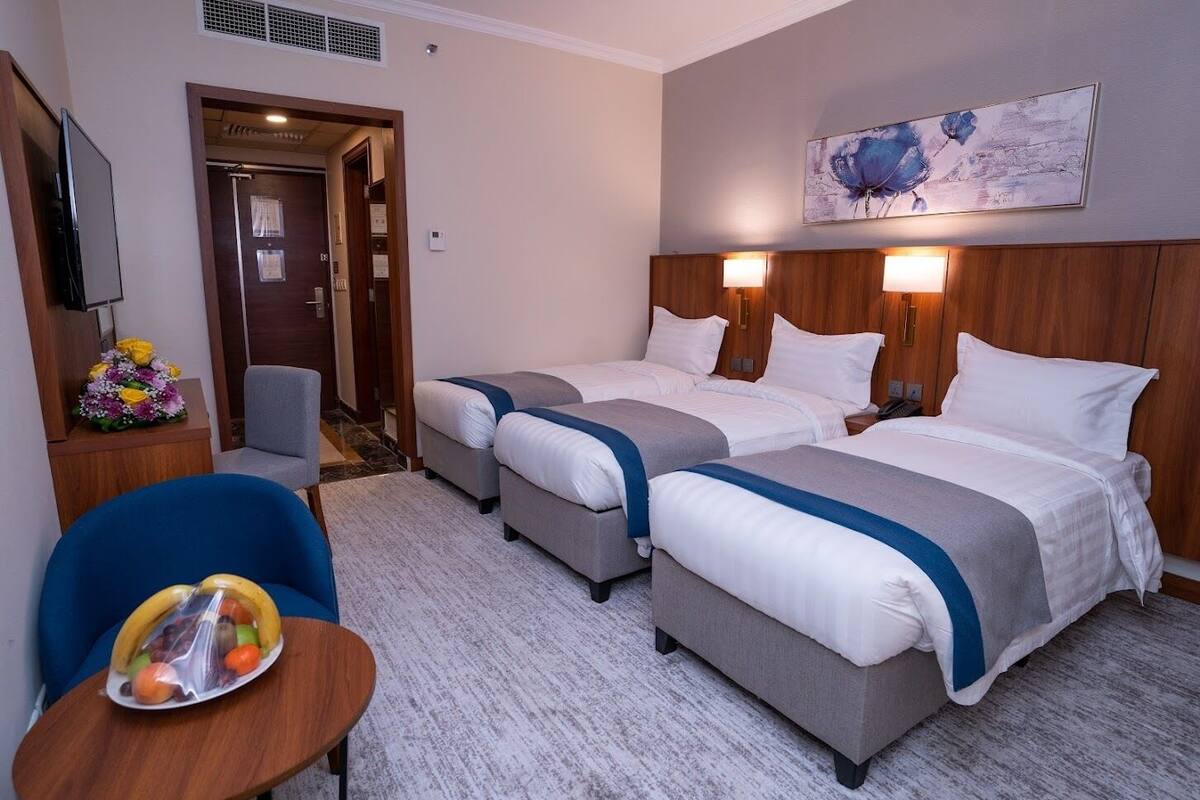 A hotel room with two beds, a desk, a chair, a fruit bowl, and a painting on the wall.