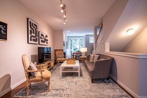 A living room with a sofa, armchair, coffee table, and artwork on the wall.