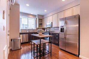 A modern kitchen with stainless steel appliances, wooden flooring, and a window providing natural light.