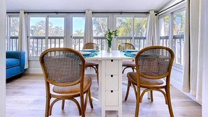 A dining area with two wicker chairs, a white table, and a vase of flowers. - Tropical Charm Steps 2 Beach/Walk 2 Bridge St (Bradenton Beach)