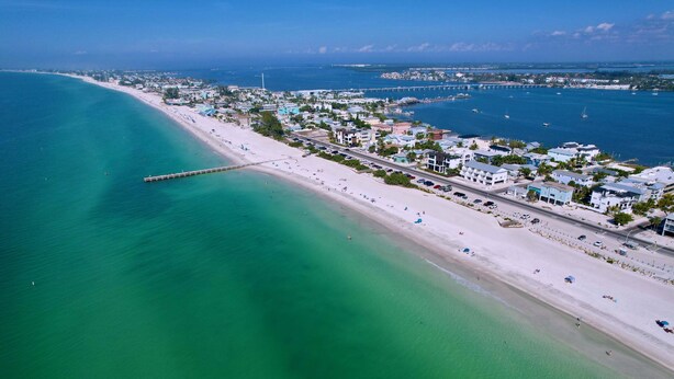 An aerial view of a coastal town with a beach, a pier, and buildings along the shore. - Tropical Charm Steps 2 Beach/Walk 2 Bridge St (Bradenton Beach)