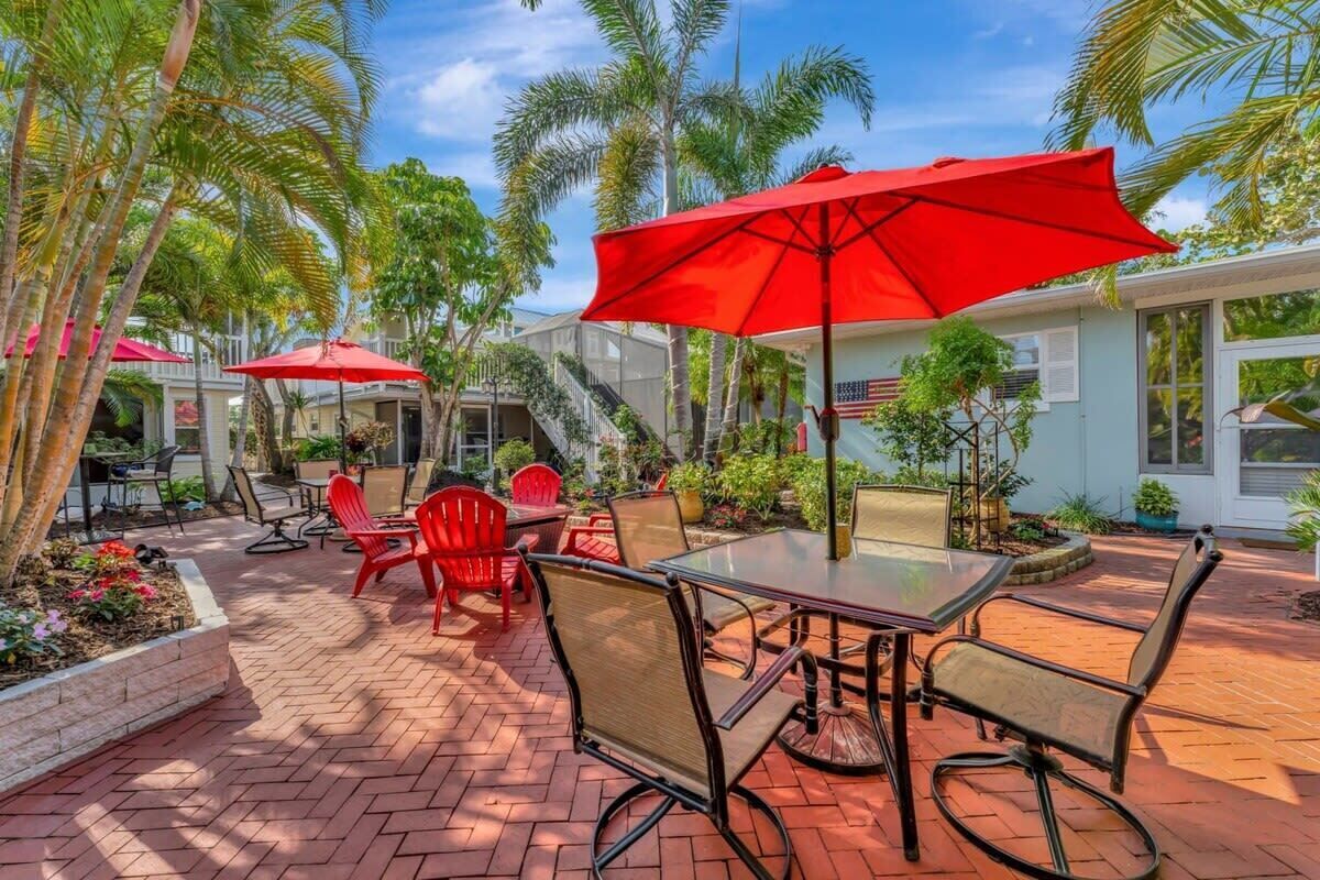 Eine Terrasse im Freien mit roten Stühlen und einem Tisch, umgeben von Palmen und einem Backsteinboden.