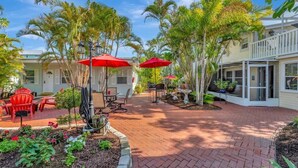 A patio area with red umbrellas, outdoor furniture, and palm trees.