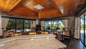 Un vaste espace de vie agrémenté d’une grande table en marbre, de sièges confortables, d’un mur décoratif en pierre et de grandes fenêtres offrant une vue sur l’extérieur.