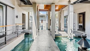 Un couloir avec une piscine, des colonnes et une vue sur l’extérieur.