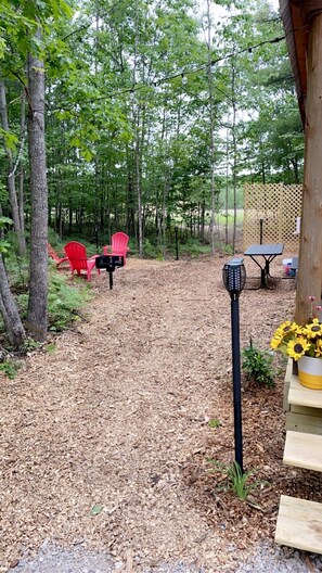 Un espace boisé doté d’une terrasse en bois, de chaises Adirondack rouges, d’une lanterne noire et d’une table agrémentée d’un arrangement de tournesols.