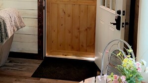 Une porte en bois avec une fenêtre, une petite table sur laquelle est posé un vase de fleurs et un banc recouvert d’une couverture.