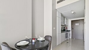A modern kitchen with stainless steel appliances, a dining area with a round table and two chairs, and a clean, minimalist design. - Chic Hotel-Style Studio in Damac Hills (Dubai)