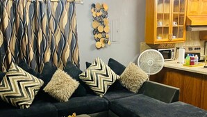 Een moderne woonkamer met een hoekbank, een klein voetenbankje en een decoratief wandkunstwerk.
