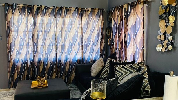 Een kamer met een moderne bank, een glazen tafel met gouden poten, en een kamerbreed gordijn.