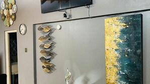 Een modern interieur met een flatscreen televisie, bevestigd boven een wand versierd met decoratieve objecten, waaronder een klok en een aantal bladachtige vormen.