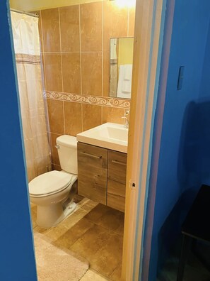 A bathroom with a toilet, sink, and shower area. - Blissett Apts your  home away from home (Kingston)
