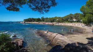 A coastal beach with clear waters, rocky shore, and a sandy beach area with people.